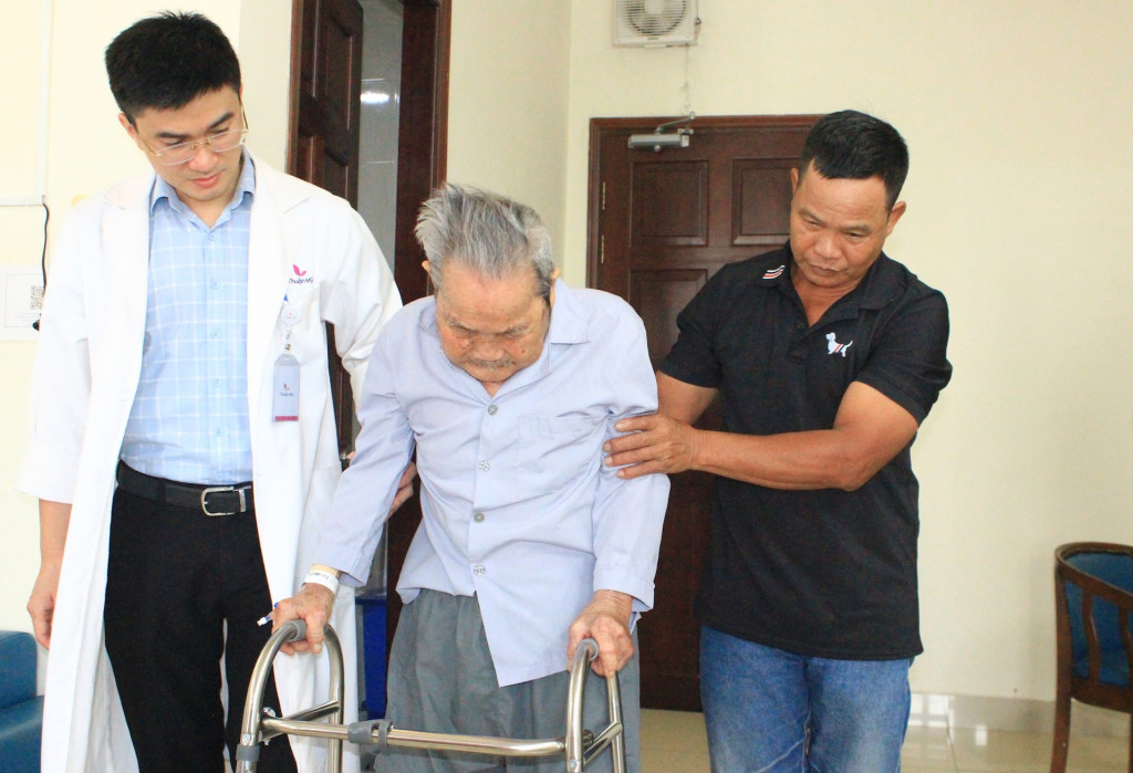 Cụ ông được bác sĩ và người nhà hỗ trợ tập đi lại sau ca phẫu thuật.