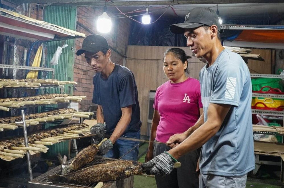 Anh Danh Khá (bìa phải, quê Bạc Liêu) lần đầu tiên lên TP.HCM phụ gia đình anh Văn Phú (bìa trái, chủ tiệm) nướng cá lóc ngày cao điểm. 