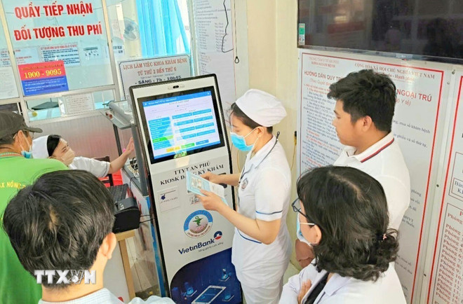 Cán bộ, nhân viên Trung tâm y tế An Phú, An Giang, hướng dẫn người dân đăng ký khám chữa bệnh bằng kiốt thông minh (Ảnh: Công Mạo/TTXVN)